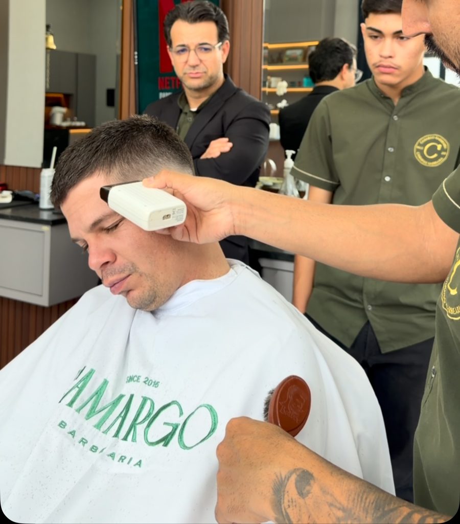 Barbeiro usando a máquina no corte, com a equipe ao fundo